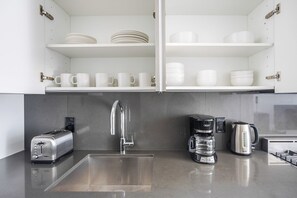 A modern kitchen with a stainless steel sink, a coffee maker, a toaster, and white cabinets with shelves above. - Blueground | Financial District, rooftop pool, nr Brooklyn Bridge (New York)