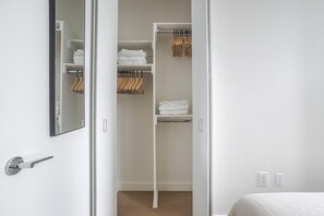 Ein weißer Kleiderschrank mit Regalen und Kleiderstange, einem Spiegel und einer Tür mit Griff.