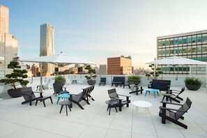 Eine Dachterrasse mit Sitzgelegenheiten im Freien, Blumentöpfen und Blick auf die Stadt.