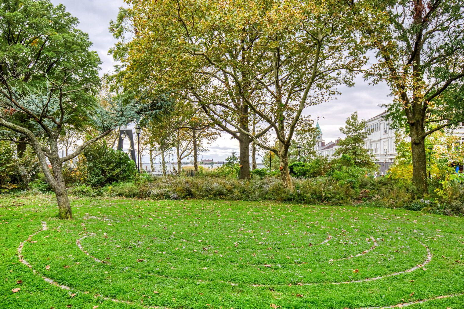 Un parque con un sendero circular, árboles y un edificio al fondo.