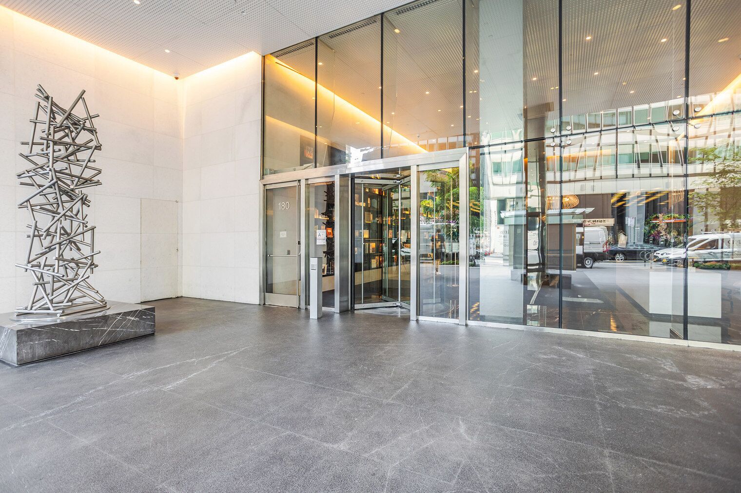A modern building entrance with a glass door, a metal sculpture, and a reflection of the interior.