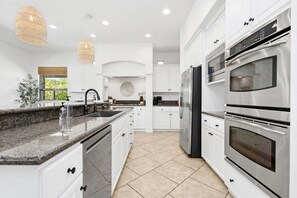 A modern kitchen with white cabinetry, stainless steel appliances, a granite countertop, and a large window. - NEW Villa Solara by GPM - Swim up bar + Games + More! Walk to festivals, Montage (Indio)