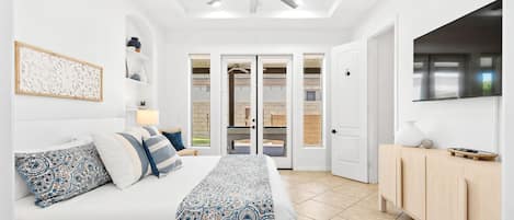 A bedroom with a bed, a ceiling fan, a TV mounted on the wall, and a door leading to a balcony.