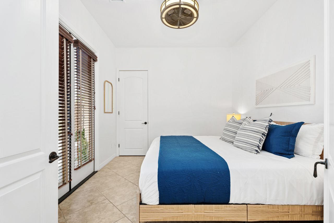 Un dormitorio con cama, una puerta y una ventana con persianas.