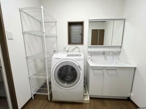 Ein kleiner Hauswirtschaftsraum mit Waschmaschine, einem Metallregal und einem Waschbecken.