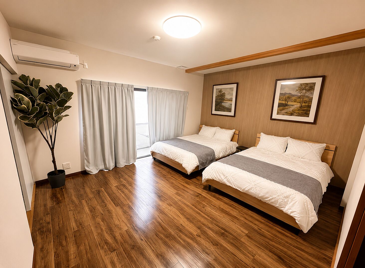 Habitación de hotel con dos camas, una planta en maceta y un amplio ventanal con cortinas.