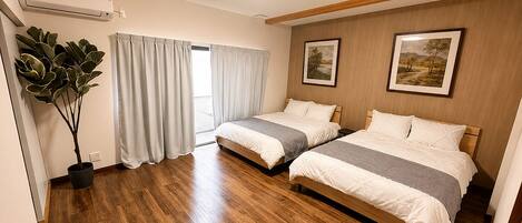 A hotel room with two beds, a potted plant, and a large window with curtains.