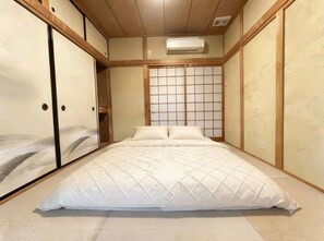 Een slaapkamer met een bed, een schuifdeur, een raam met een rasterpatroon en een airconditioning.
