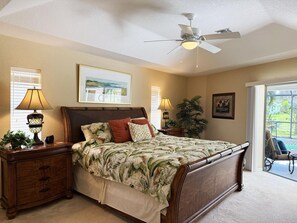 A bedroom with a bed, nightstands, a ceiling fan, and a view through a glass door. - 3BR Heated Pool Villa - Golf & Beaches (Rotonda West)