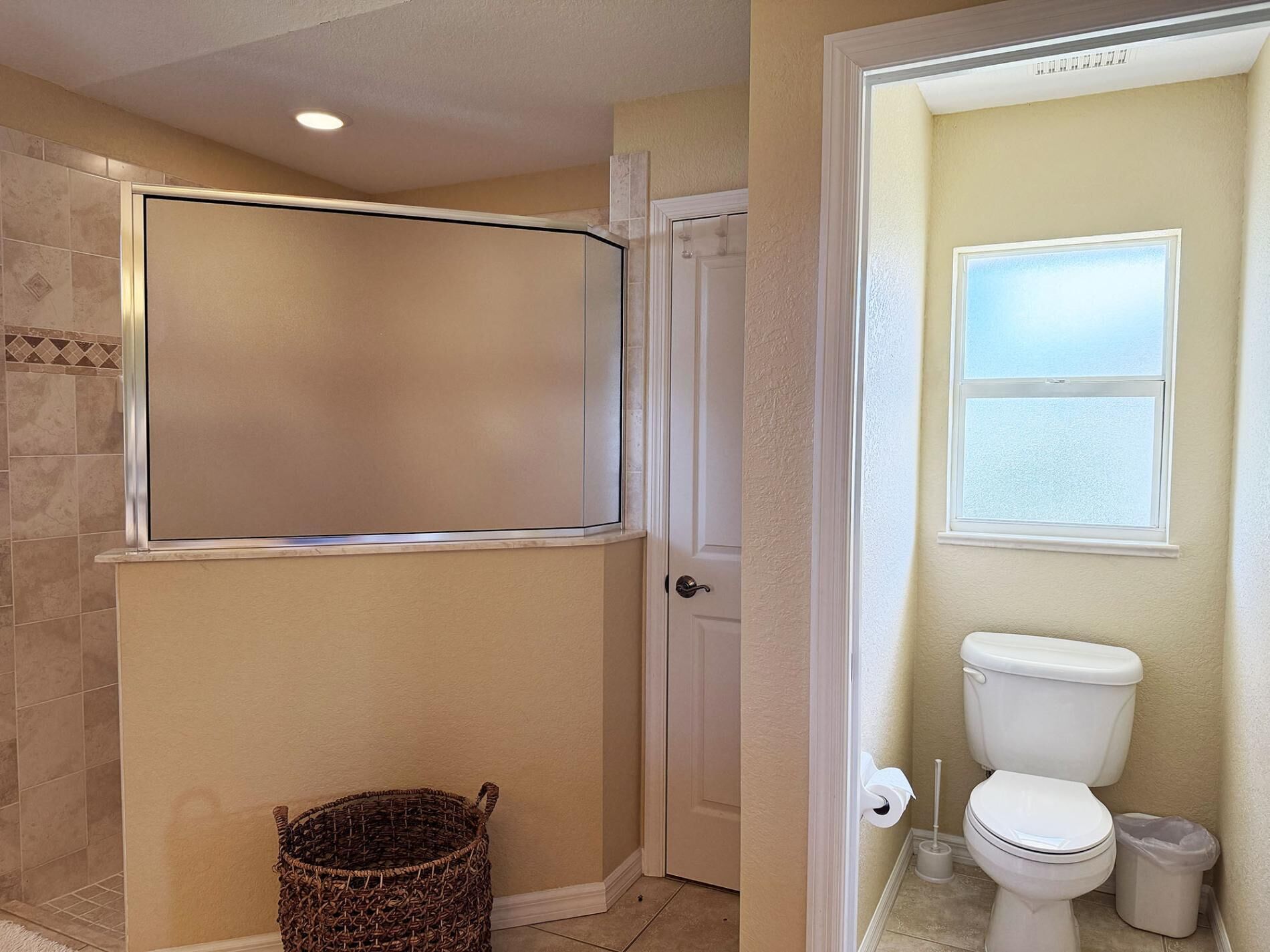 Une salle de bain comprenant des toilettes, une fenêtre, un espace douche et une poubelle.