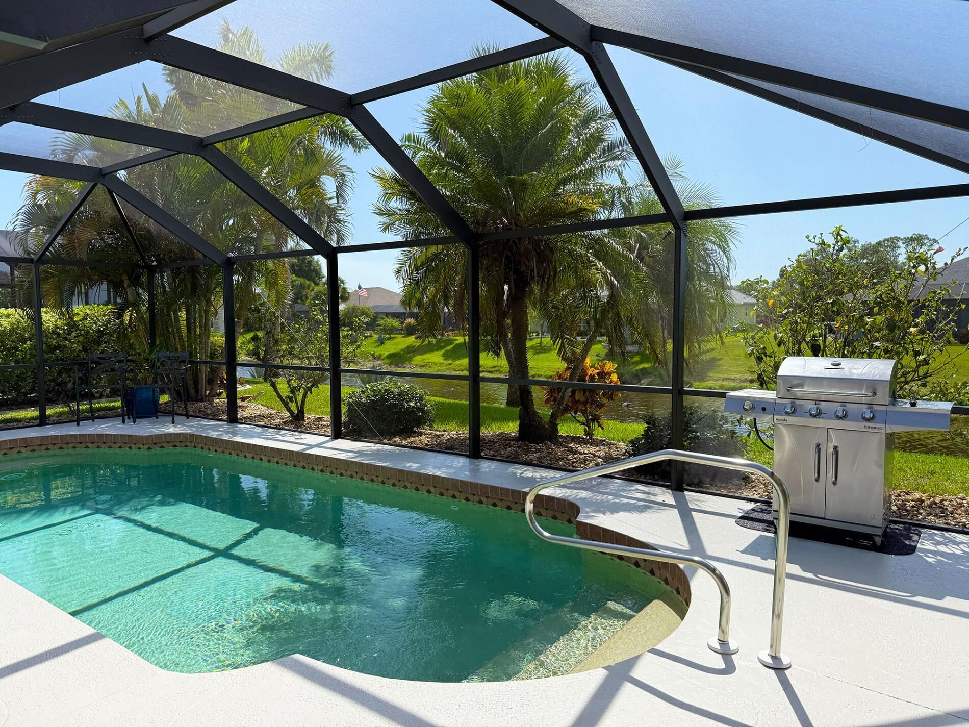 A pool area with a clear view of the surrounding landscape, including palm trees and a grassy area.