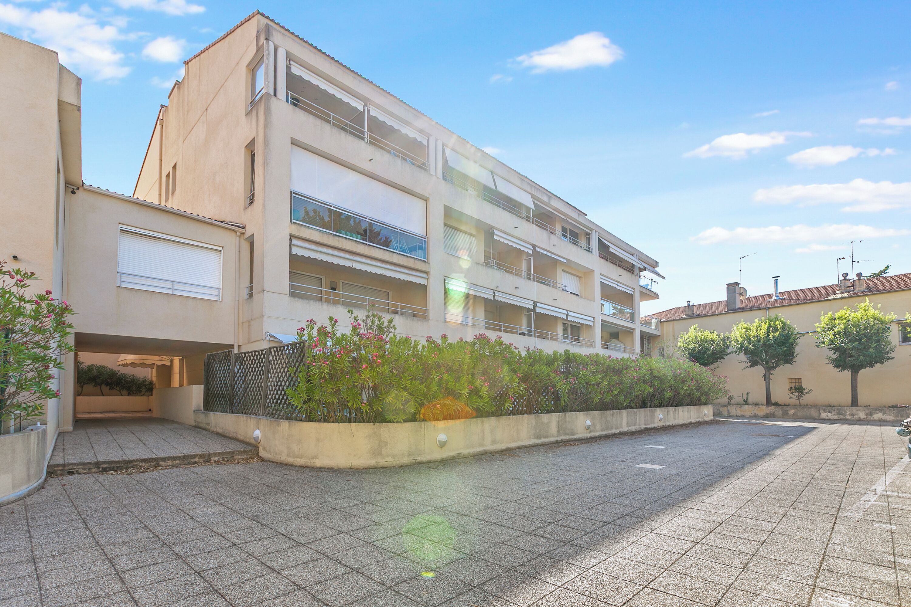 A multi-story residential building with balconies, a paved courtyard, and surrounding greenery.