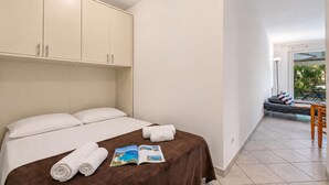 A hotel room with a bed, a magazine, and a view of the outdoor seating area. - Appartement Les Jasmins, Beaulieu sur Mer, France (Beaulieu sur Mer)
