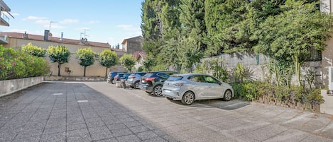 A parking area with several cars parked in a row, surrounded by greenery and buildings.