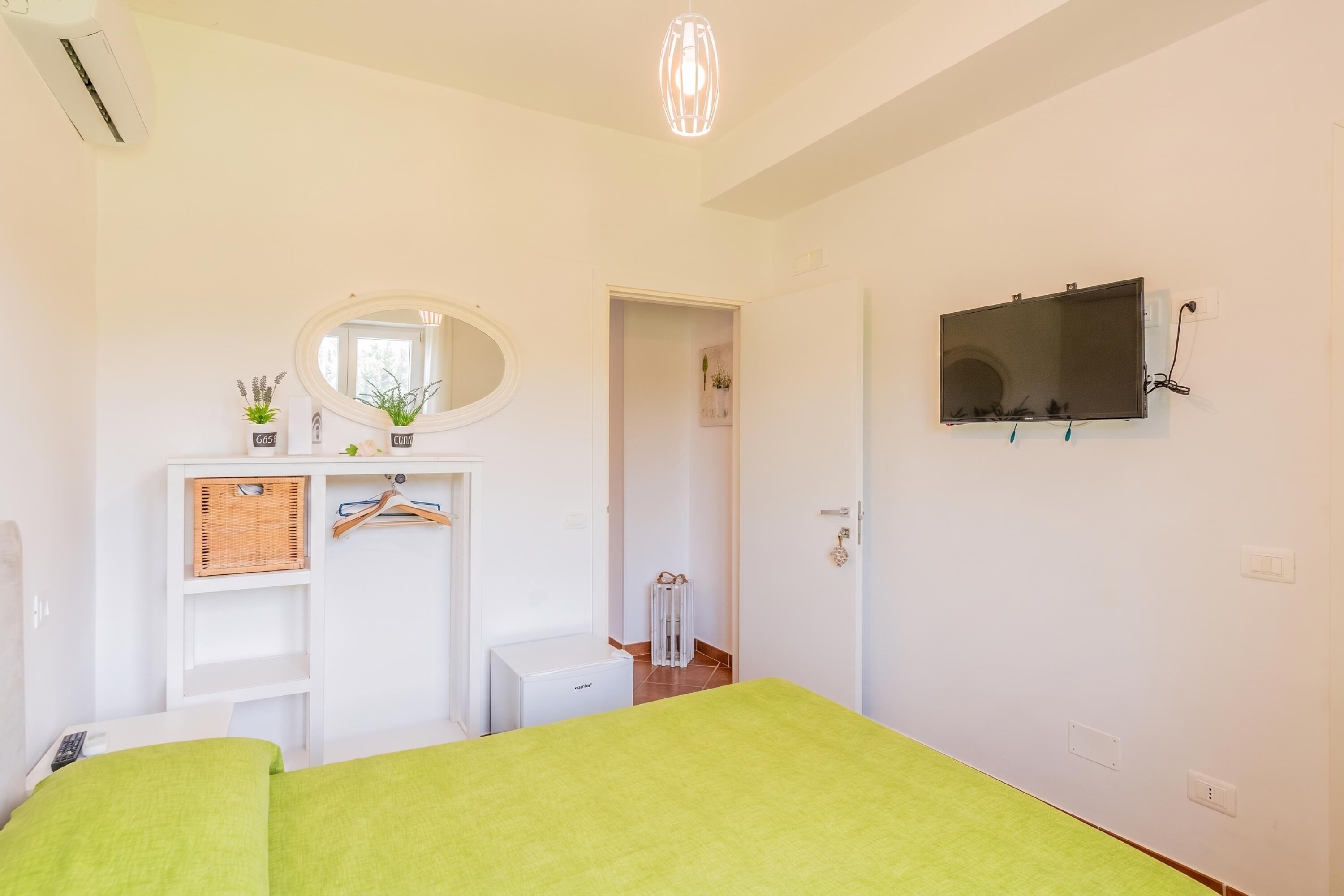 Un dormitorio con cama, cómoda, espejo, televisor y radiador.