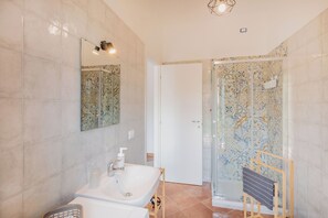 Een badkamer met een wit wastafelmeubel, een spiegel, een douche met betegelde wanden en een handdoekrek.
