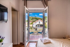 Une chambre avec balcon, un lit, une télévision et une vue sur une colline.