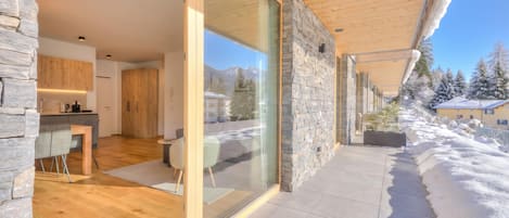 A modern interior with a stone facade, wooden flooring, and a glass door leading to a snowy outdoor area.