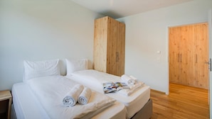 Una cama doble con ropa de cama blanca, un armario de madera y una puerta de madera.
