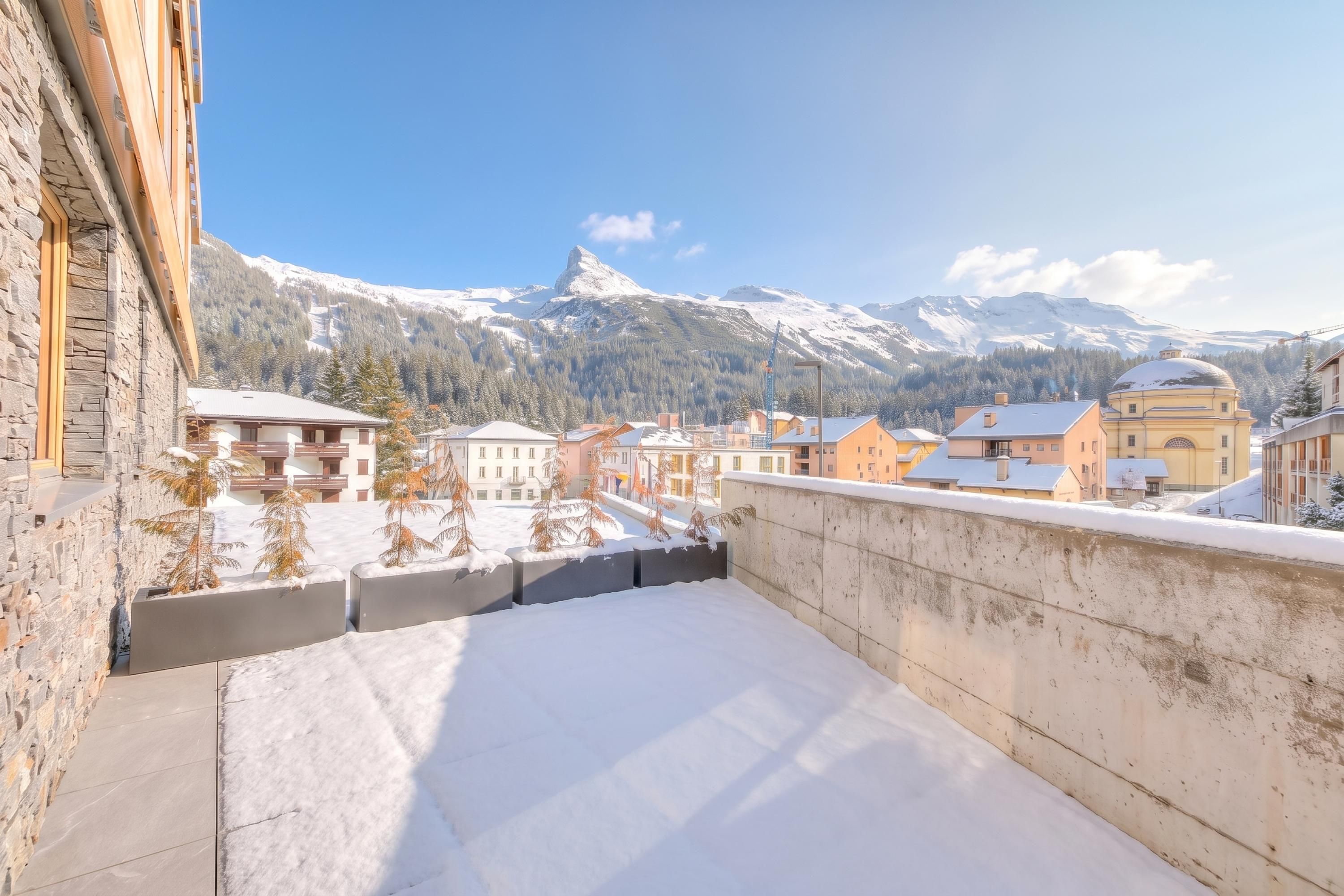 A balcony with a snow-covered ground, overlooking a town with buildings and a mountain in the background.