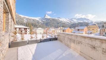 A balcony with a snow-covered ground, overlooking a town with buildings and a mountain in the background.