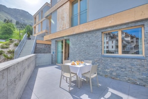 A modern building with a stone facade, a balcony with a table set for breakfast, and a staircase leading to an upper level. - Residenza Castanea 001 Modern Alpine Stay In San Bernardino | Ski, Hiking & Nature, San Bernardino, Switzerland (San Bernardino)