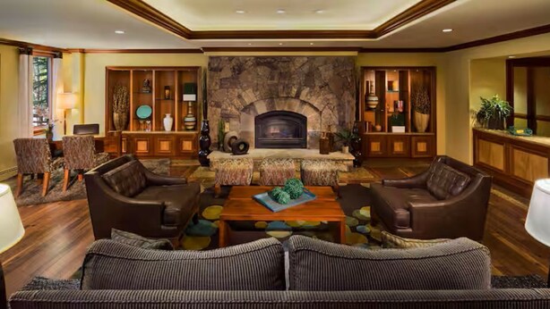 Ein großzügiges Wohnzimmer mit Kamin, Ledersofas, einem Couchtisch und einer Wand aus Naturstein.