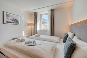 A hotel room with two beds, a window with curtains, a bedside lamp, and a framed picture on the wall. - Residenza Larix 105 San Bernardino Alpine Apartments, San Bernardino, Switzerland (San Bernardino)