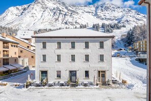 A multi-story building with a flat roof, surrounded by snow-covered ground and mountains in the background. - Residenza Larix 002 San Bernardino Alpine Apartments, San Bernardino, Switzerland (San Bernardino)