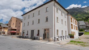 A multi-story hotel with a flat facade, large windows, and a ground-level outdoor seating area with tables and chairs. - Residenza Larix 103 Modern Alpine Stay In San Bernardino | Ski, Hiking & Nature, San Bernardino, Switzerland (San Bernardino)