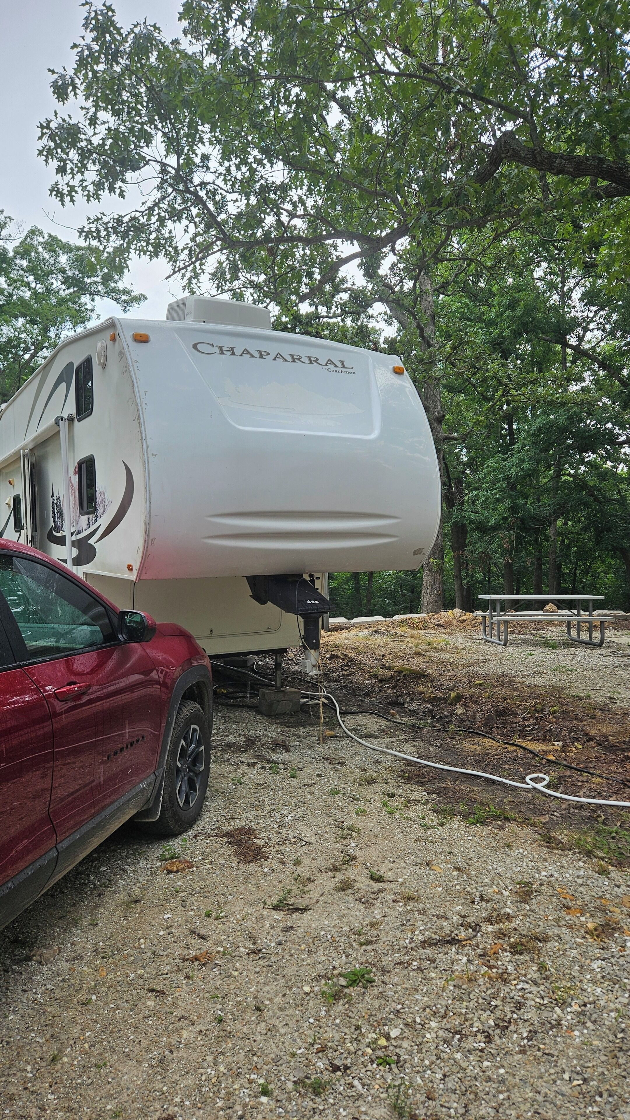 En hvid campingvogn med teksten 'CHAPARRAL' på siden, parkeret på en grusoverflade med træer i baggrunden.
