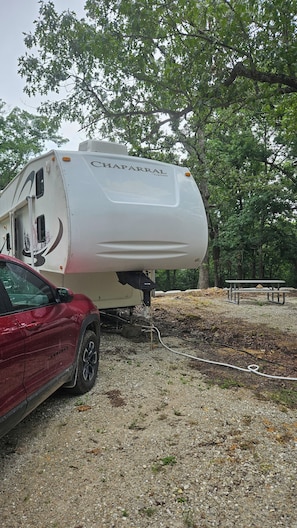 A white RV with 'CHAPARRAL' written on the side parked on a gravel surface with trees in the background.
