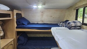 A small, compact room with bunk beds, a shelf with folded clothes, and a window providing a view outside. - Camper 6 Enjoyable 2-bedroom recreational vehicle with AC just out of Fair Play. (Fair Play)