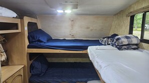 Ein kleiner, kompakter Raum mit Etagenbetten, einem Regal mit zusammengelegter Kleidung und einem Fenster mit Ausblick.