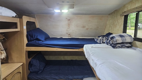 A small, compact room with bunk beds, a shelf with folded clothes, and a window providing a view outside.
