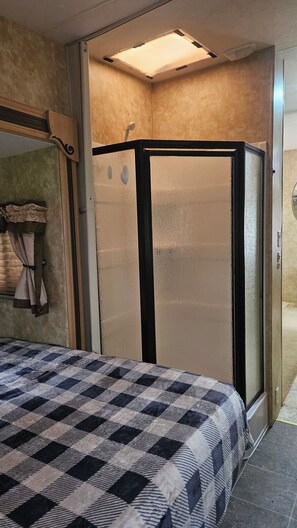 Quarto de hotel com cama, box de chuveiro e janela.