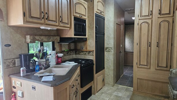 A compact kitchen with wooden cabinets, a black stove, and a refrigerator. - Camper 6 Enjoyable 2-bedroom recreational vehicle with AC just out of Fair Play. (Fair Play)