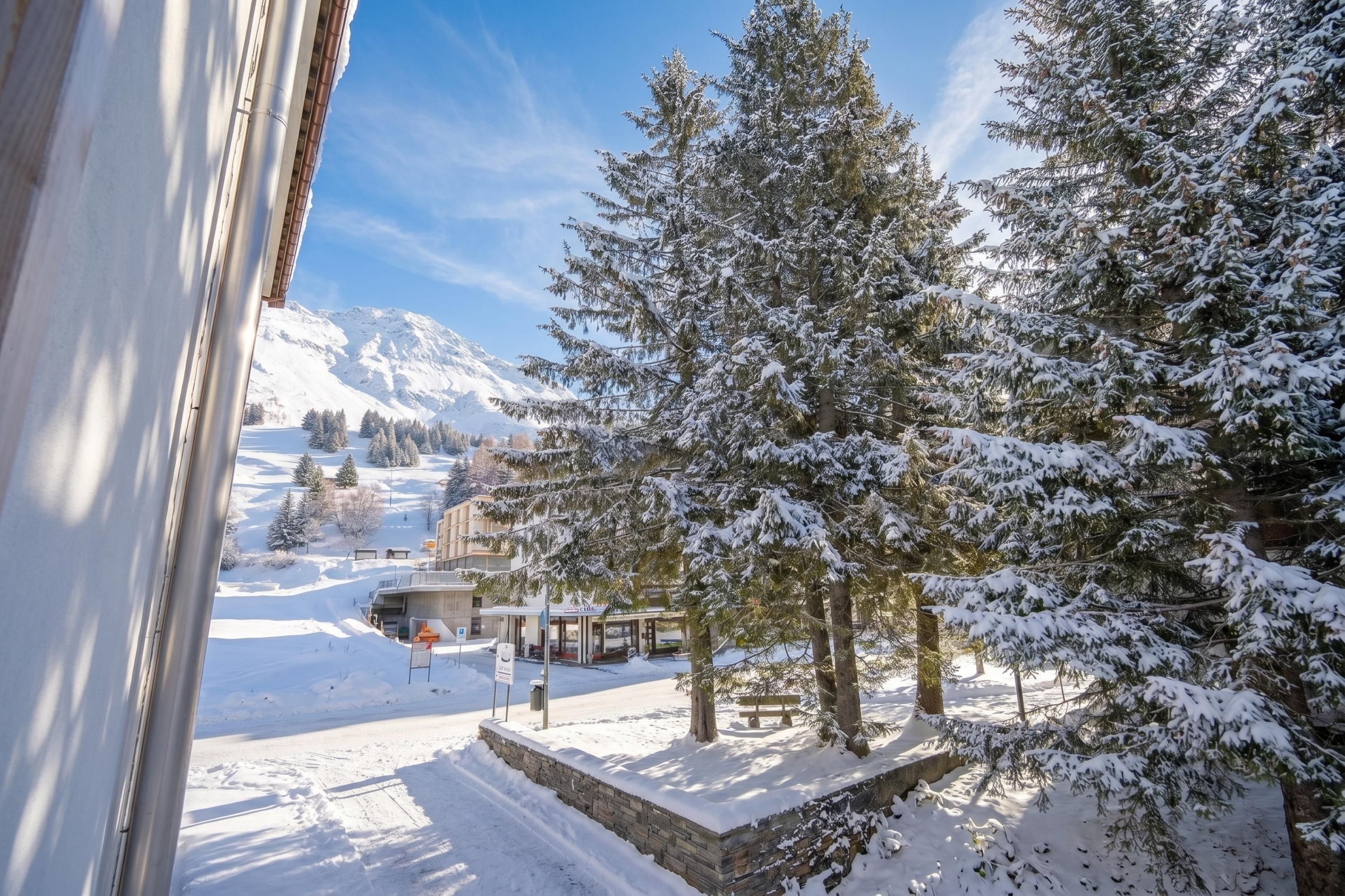 Schneebedeckte Landschaft mit einem Berg im Hintergrund, einem Gebäude mit einer Beschilderung und verschneiten Bäumen.