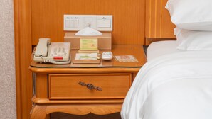 A hotel room with a wooden nightstand, a telephone, a tissue box, a remote control, and a bed with white bedding. - Vienna Guangzhou Beijing Rd Gongyuanqian (Guangzhou)
