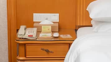 A hotel room with a wooden nightstand, a telephone, a tissue box, a notepad, and a small clock.