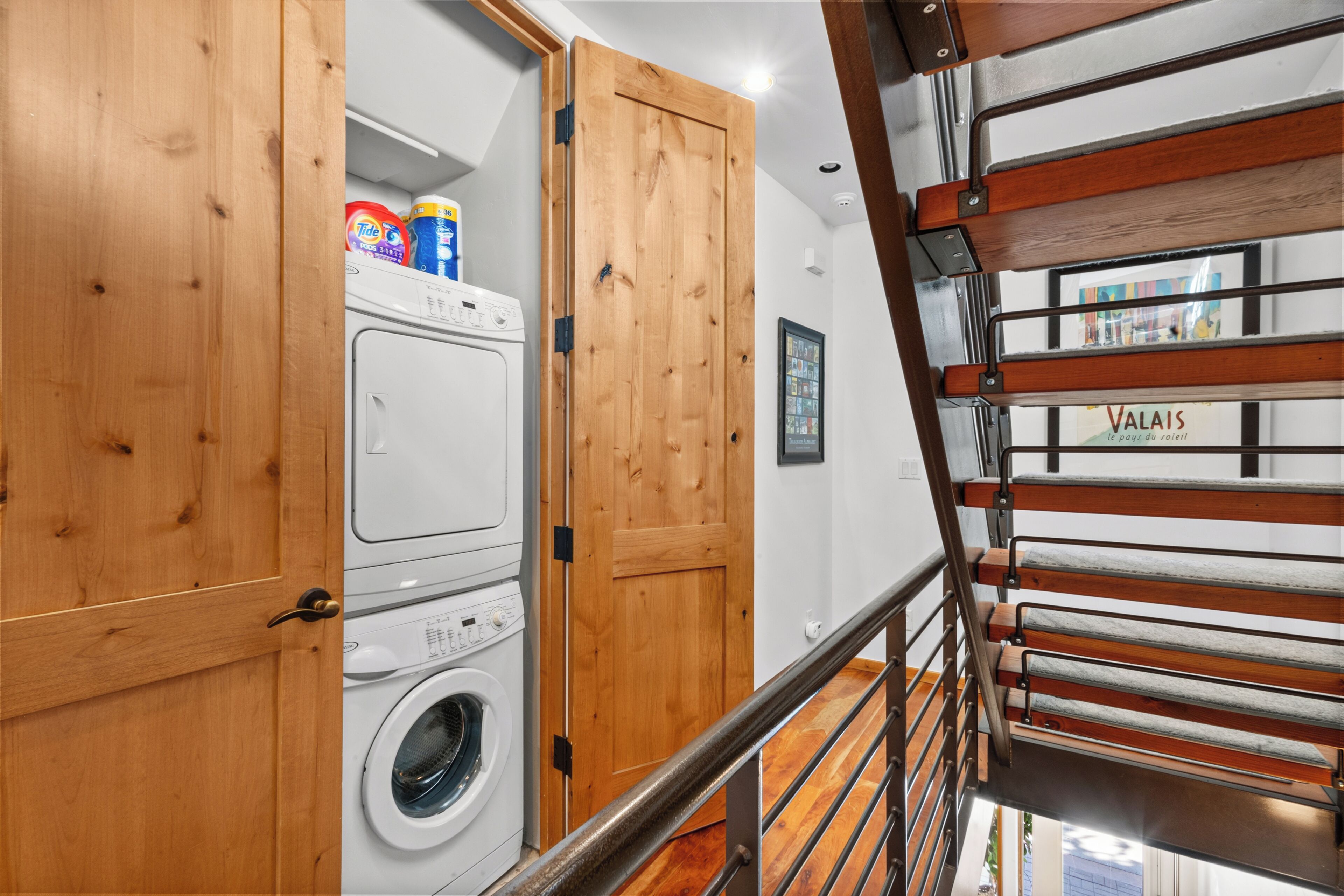 A laundry room with a washing machine and a dryer, wooden cabinets, and a metal staircase.