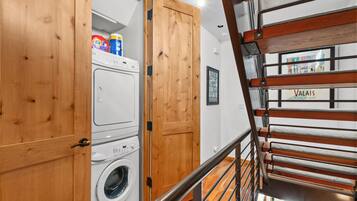 A laundry room with a washing machine and a dryer, wooden cabinets, and a metal staircase.