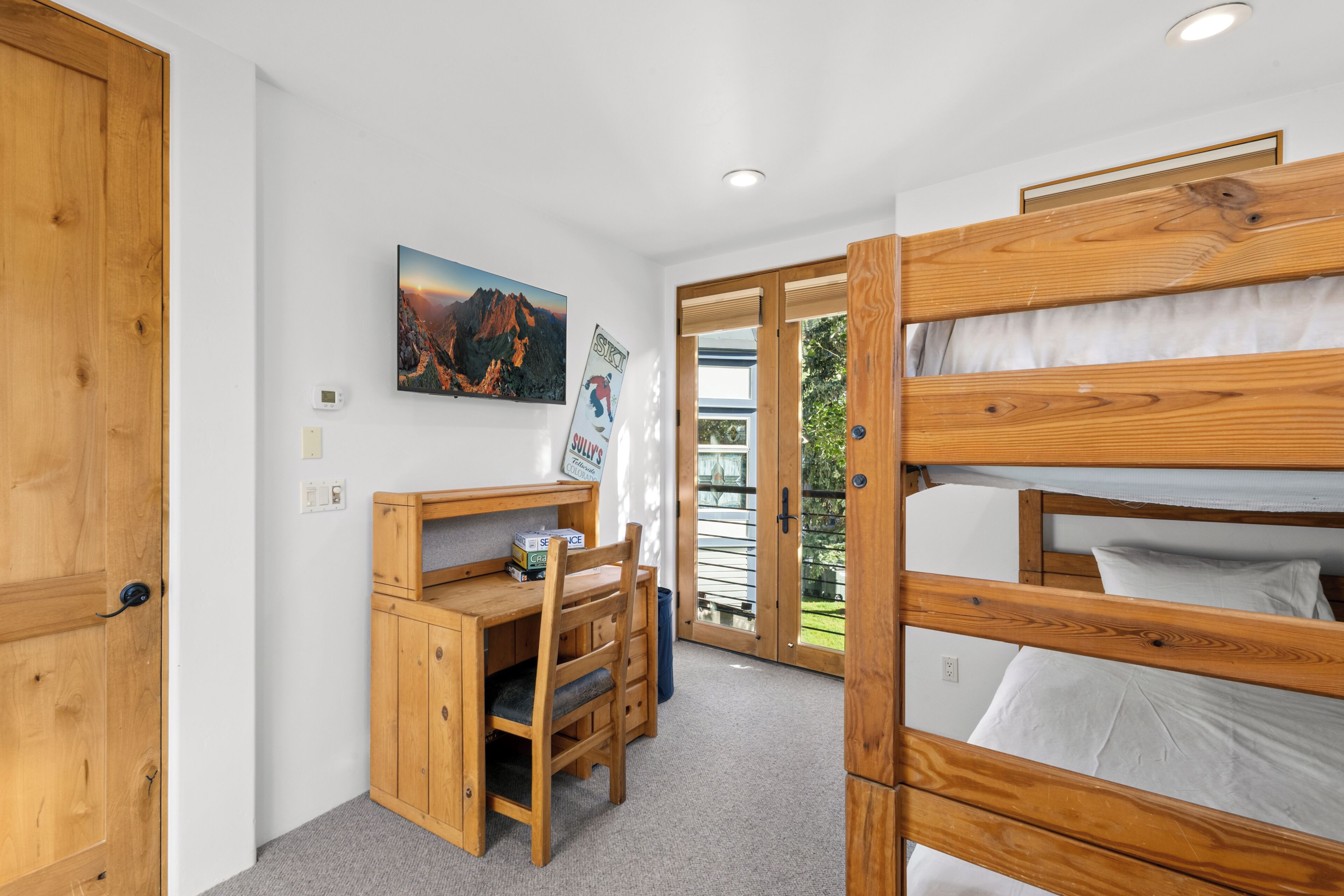A room with a bunk bed, a desk with a chair, a television, and a window with a view of the outdoors.