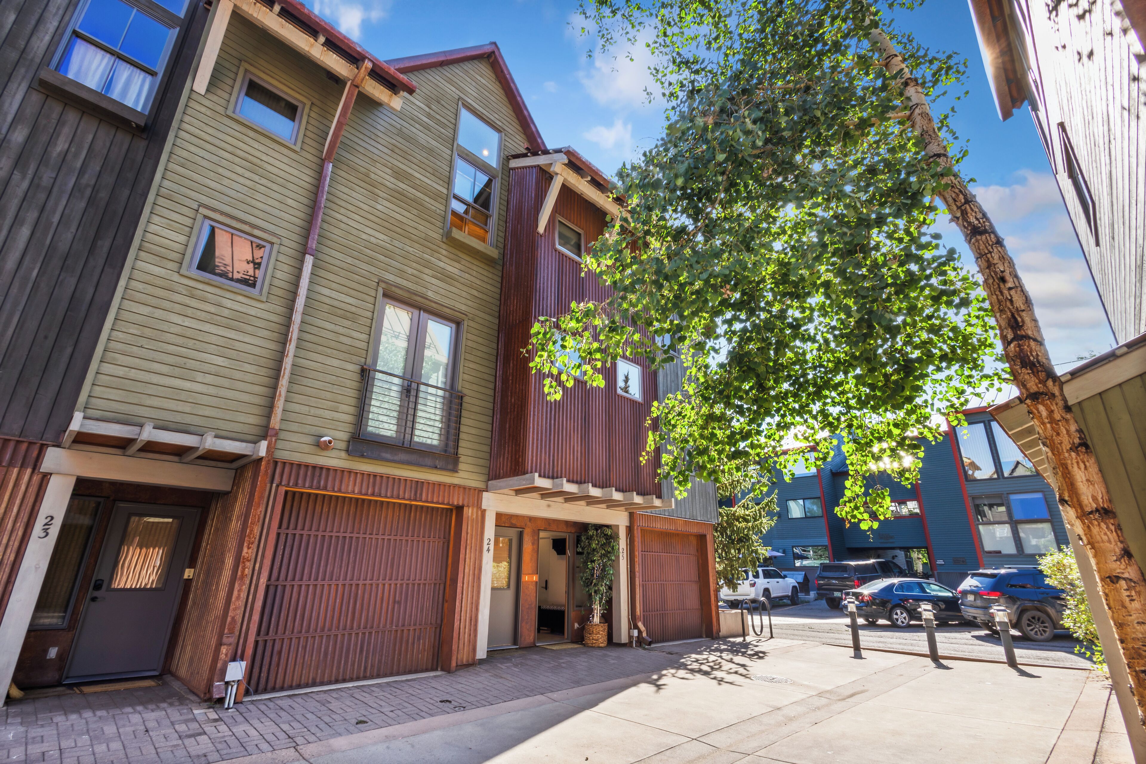 A multi-story residential building with a garage entrance, a tree in front, and parked cars.
