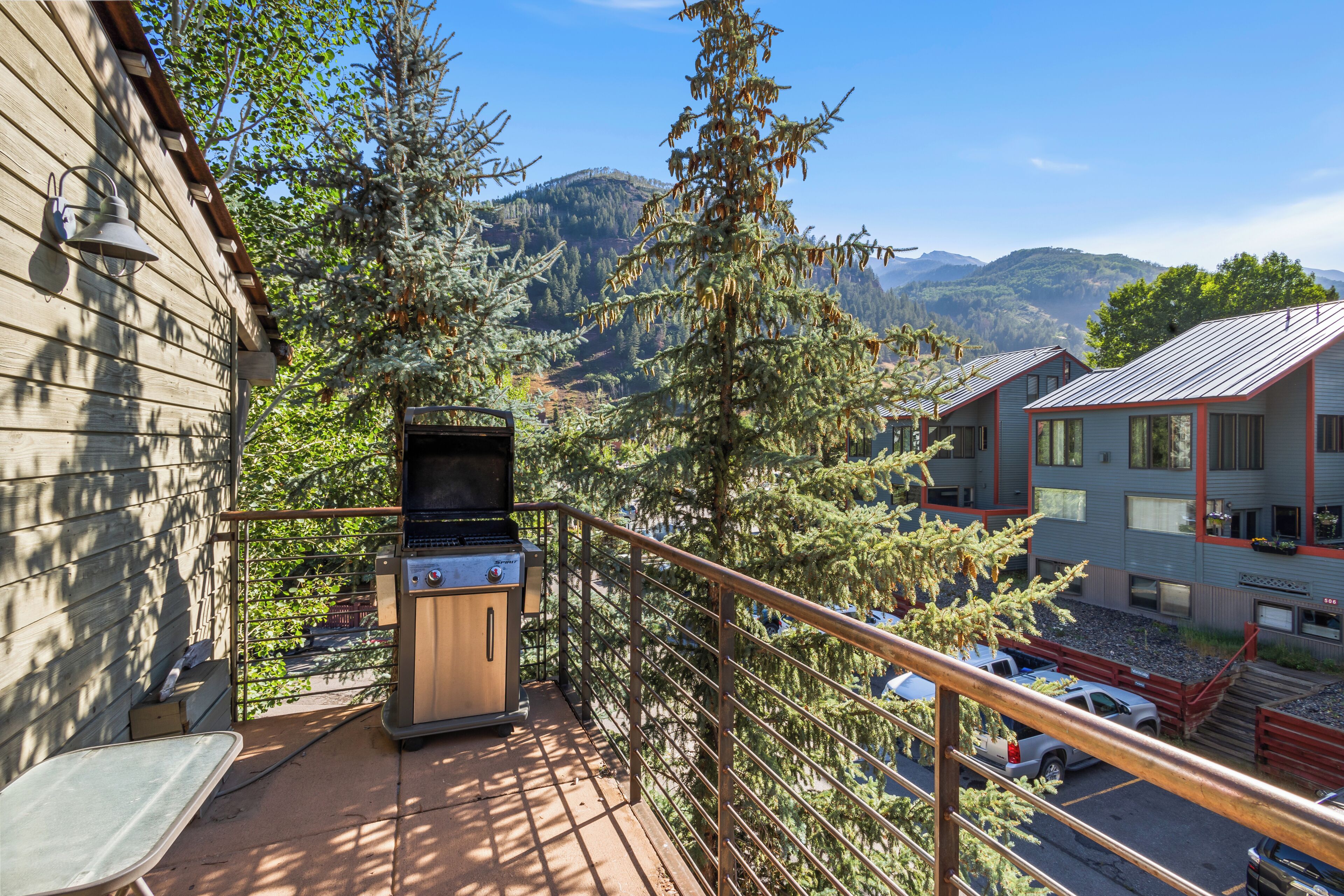 A balcony with a grill, overlooking a mountainous landscape and a residential area.