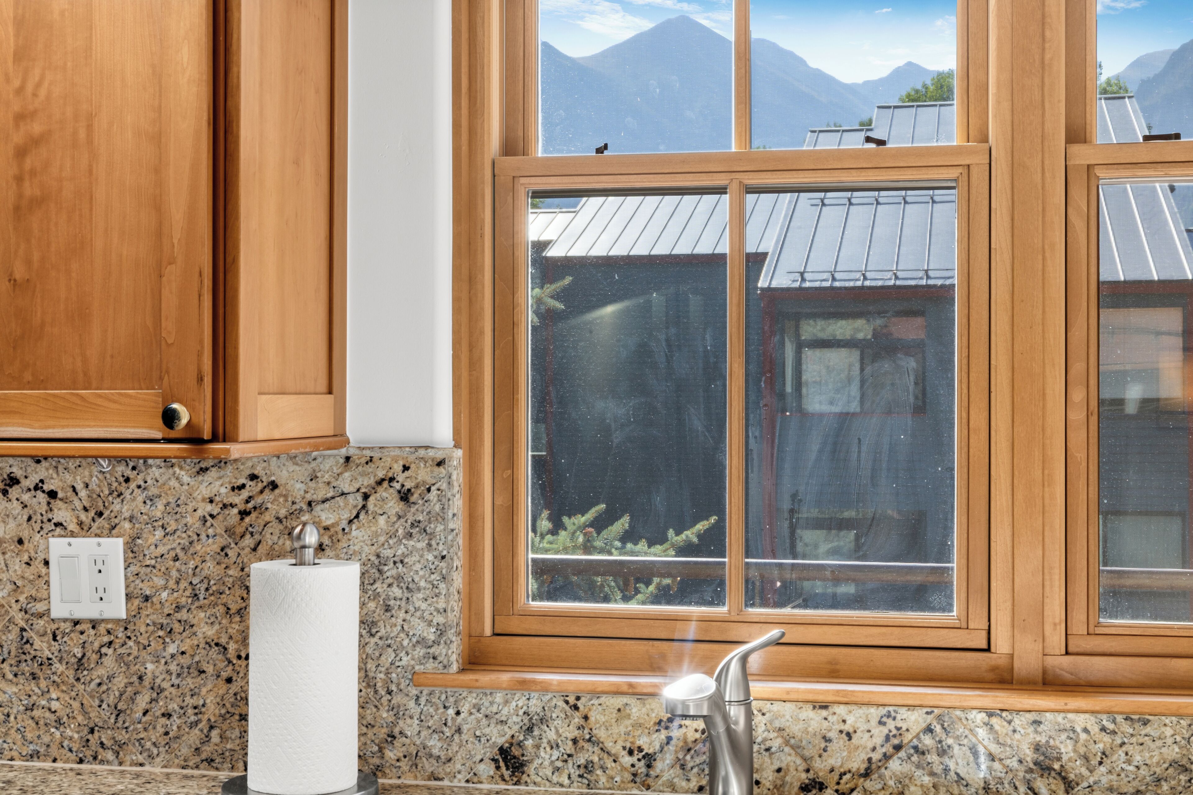 Une cuisine dotée de plans de travail en granit, d’armoires en bois, d’un robinet en acier inoxydable et d’une fenêtre offrant une vue sur les montagnes.