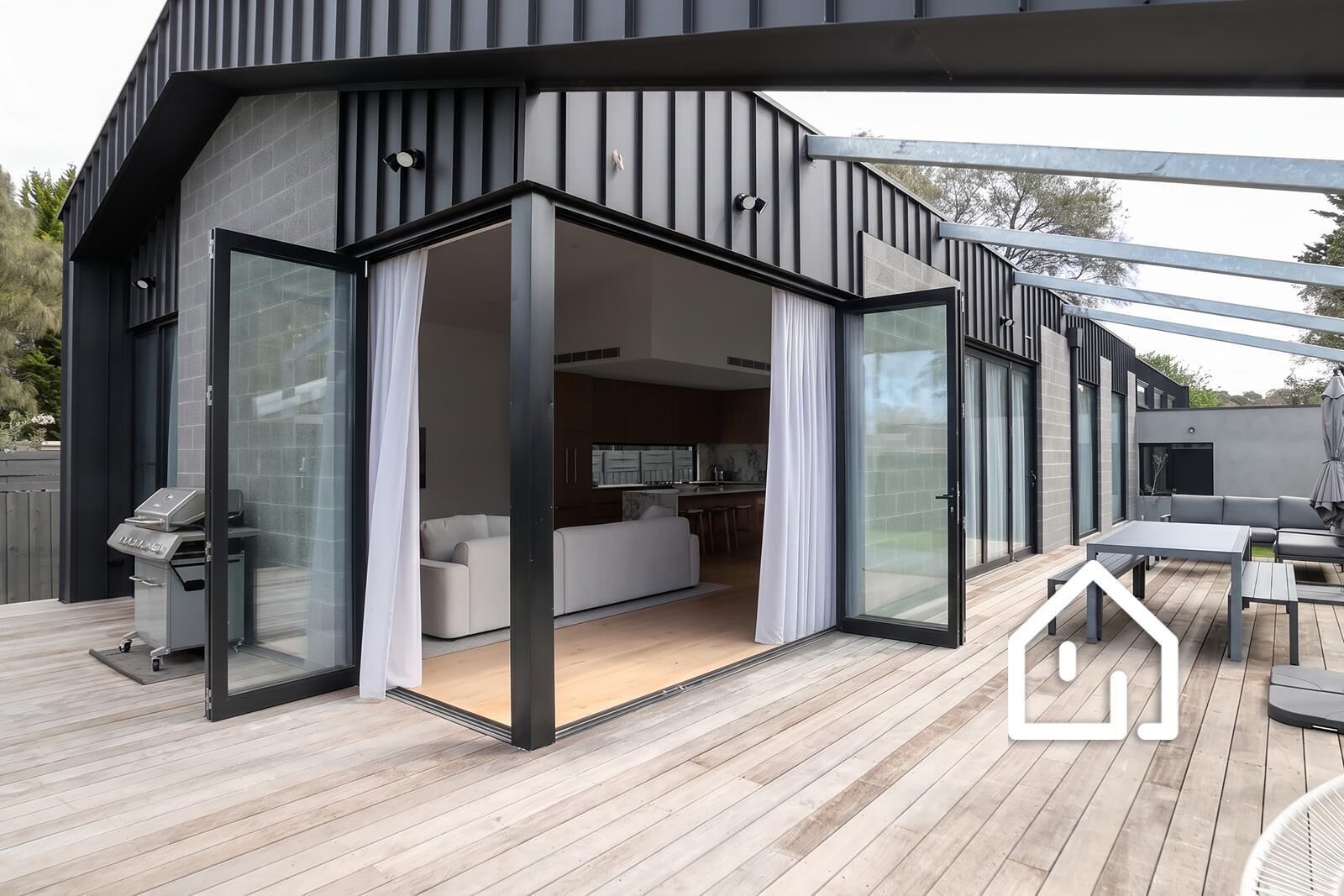 Een modern huis met een terras, schuifdeuren die leiden naar een woonruimte met een bank en een eettafel.
