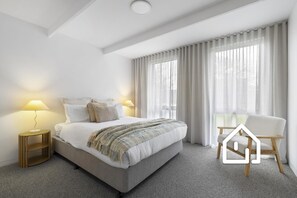A modern hotel room with a bed, two bedside lamps, a chair, and a view of the outdoors through large windows. - Elements of Rye *1 NIGHT FREE* (Rye)