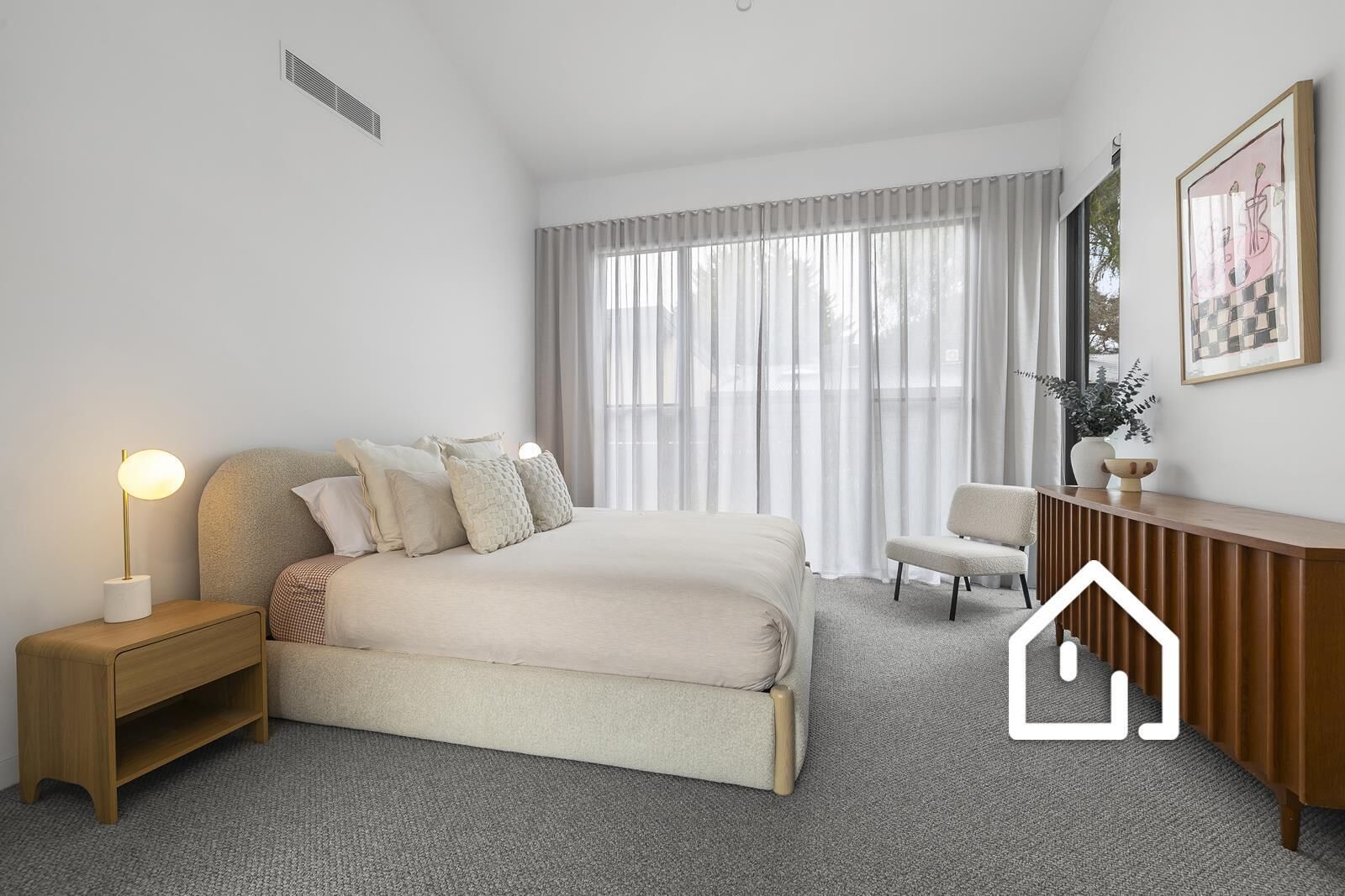 A modern bedroom with a bed, bedside table, chair, and a desk with a plant.