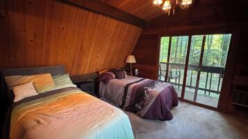 Ein Schlafzimmer in einer Hütte mit zwei Betten, einem Deckenventilator und einem großen Fenster mit Blick auf einen Wald.